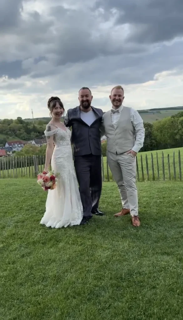 Brautpaar und Hochzeitsmoderator auf einer Wiese mit Blick auf die Hügel
