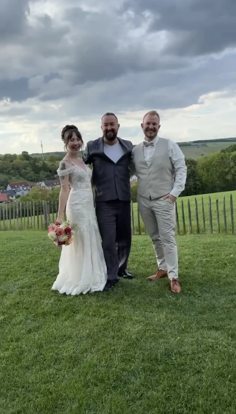 Brautpaar und Hochzeitsmoderator auf einer Wiese mit Blick auf die Hügel