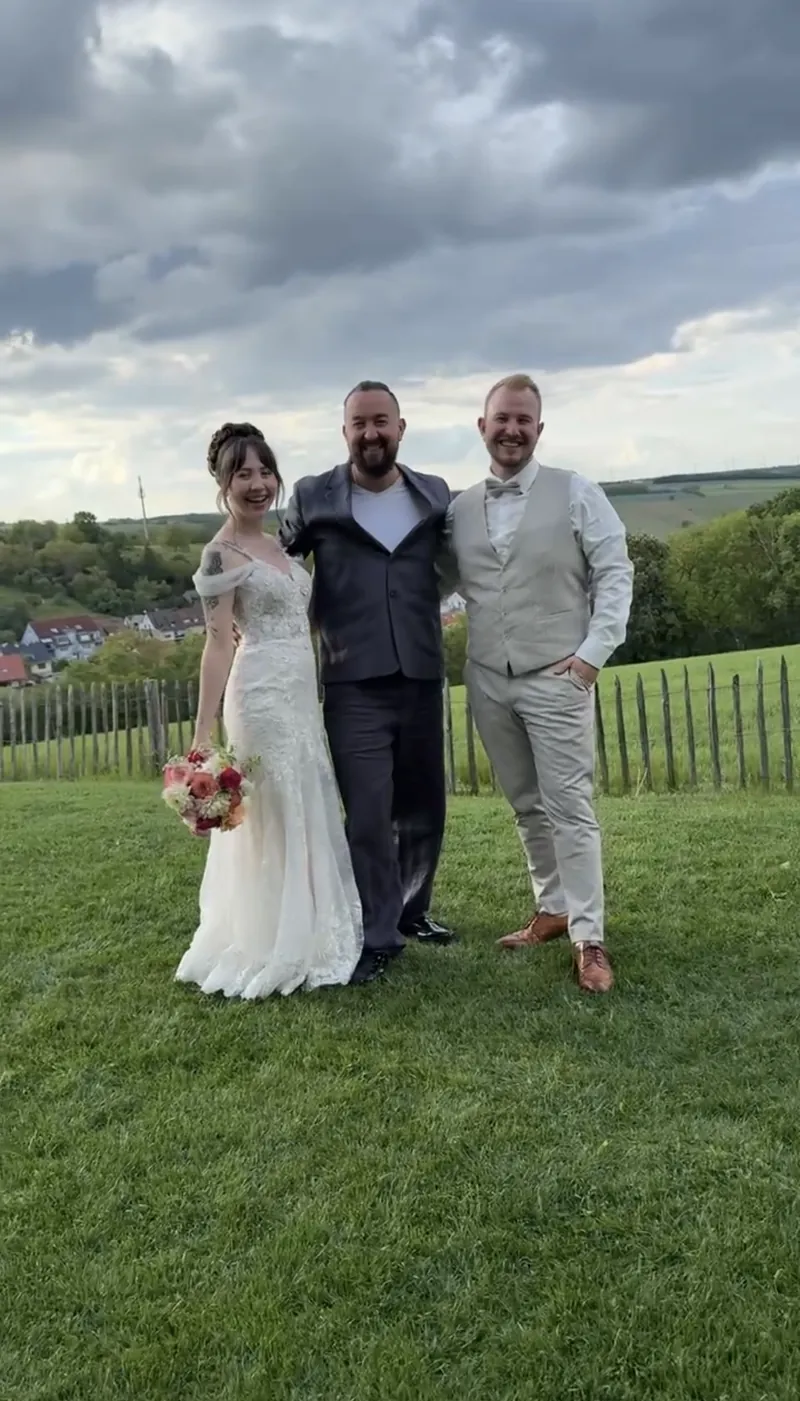 Brautpaar und Hochzeitsmoderator auf einer Wiese mit Blick auf die Hügel Brautpaar und Hochzeitsmoderator auf einer Wiese mit Blick auf die Hügel