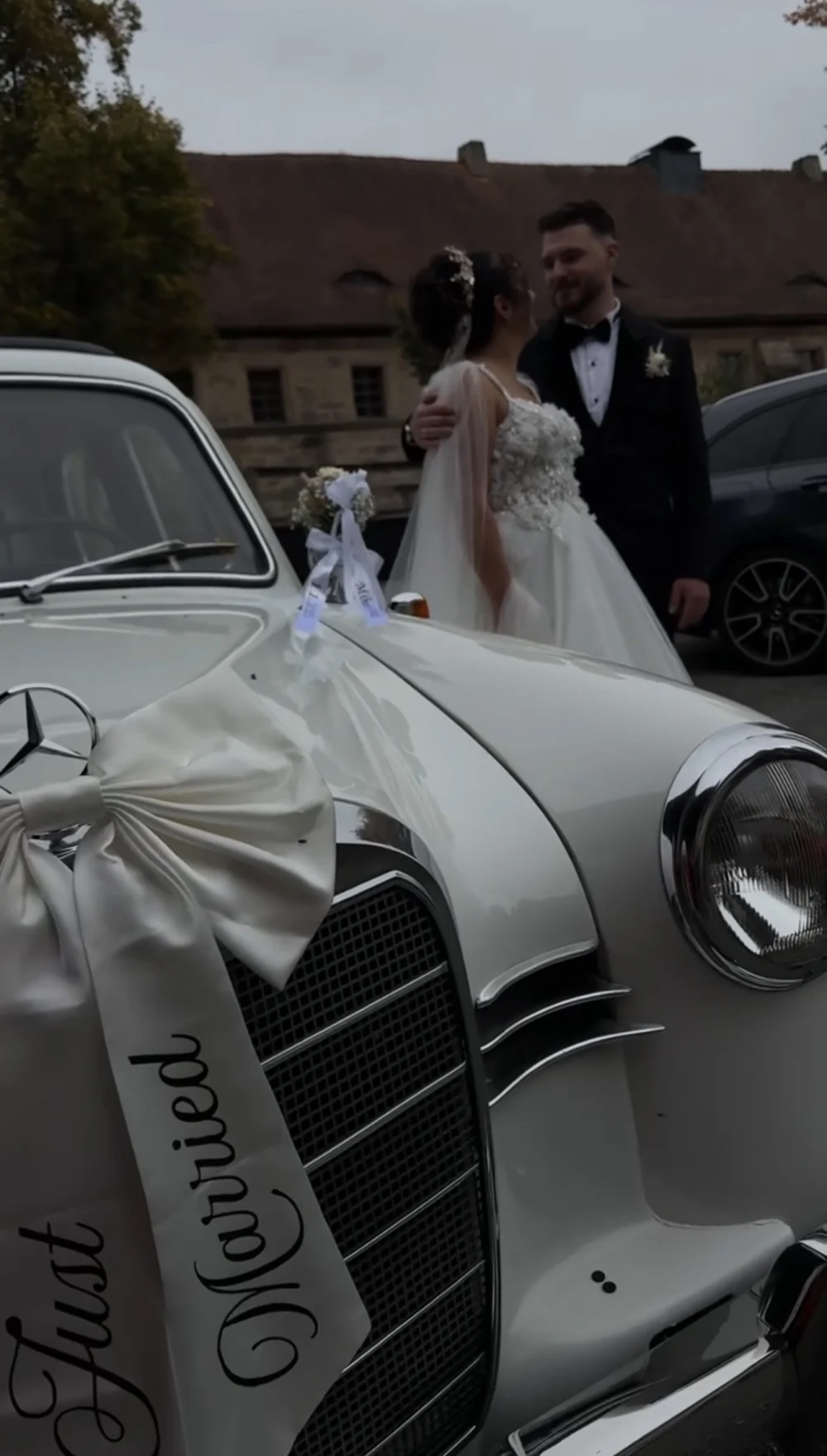 Hochzeitsauto mit Schleife Just Married, das Brautpaar im Hintergrund Hochzeitsauto mit Schleife Just Married, das Brautpaar im Hintergrund
