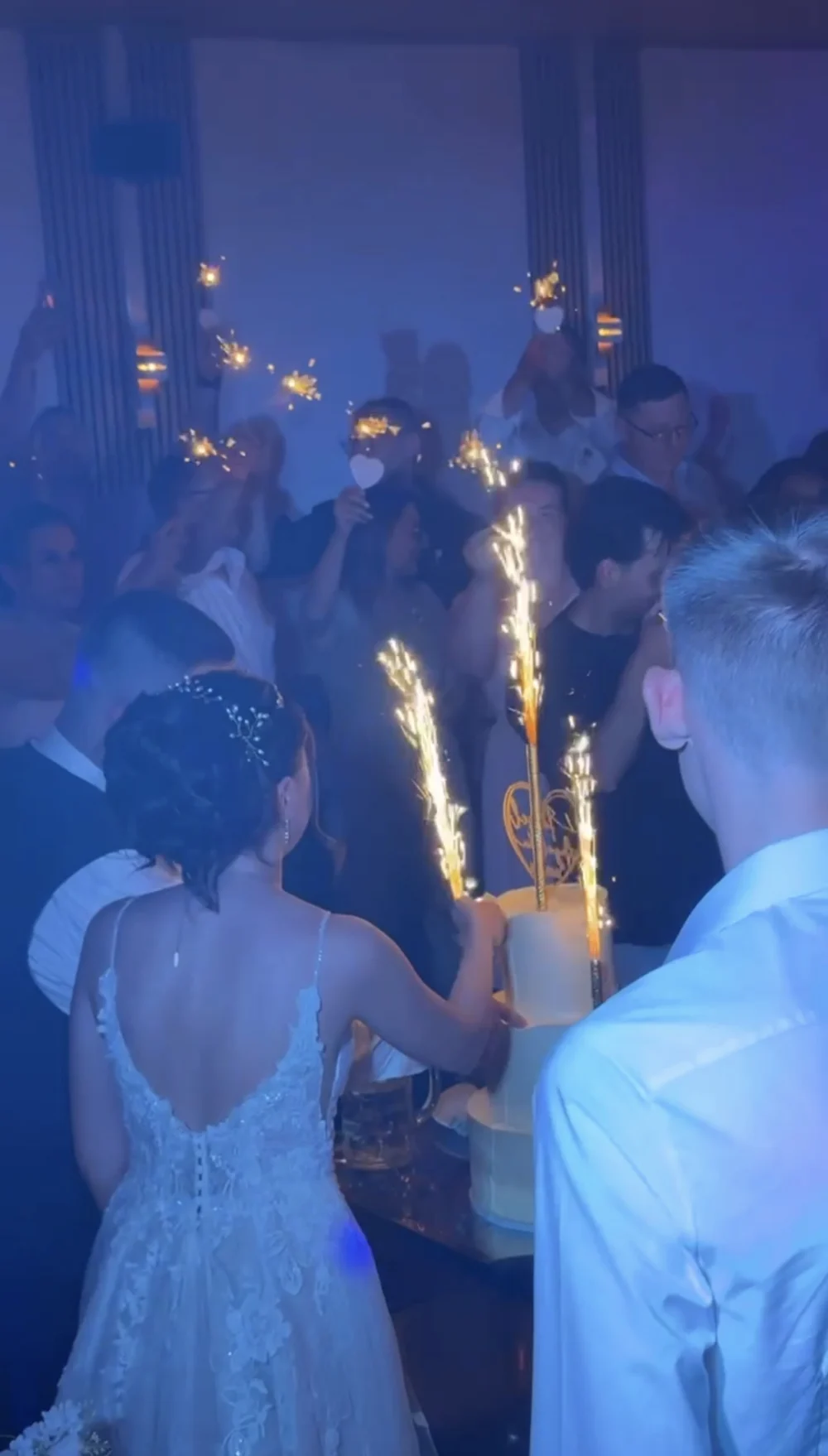 Hochzeitstorte mit Wunderkerzen, Gäste feiern im blauen Licht Hochzeitstorte mit Wunderkerzen, Gäste feiern im blauen Licht